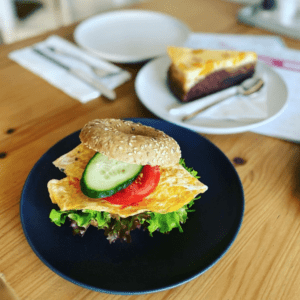Unprofessionelles Foto gedeckter Tisch, Bagel mit Omelette, im Hintergrund ein Stück Kuchen