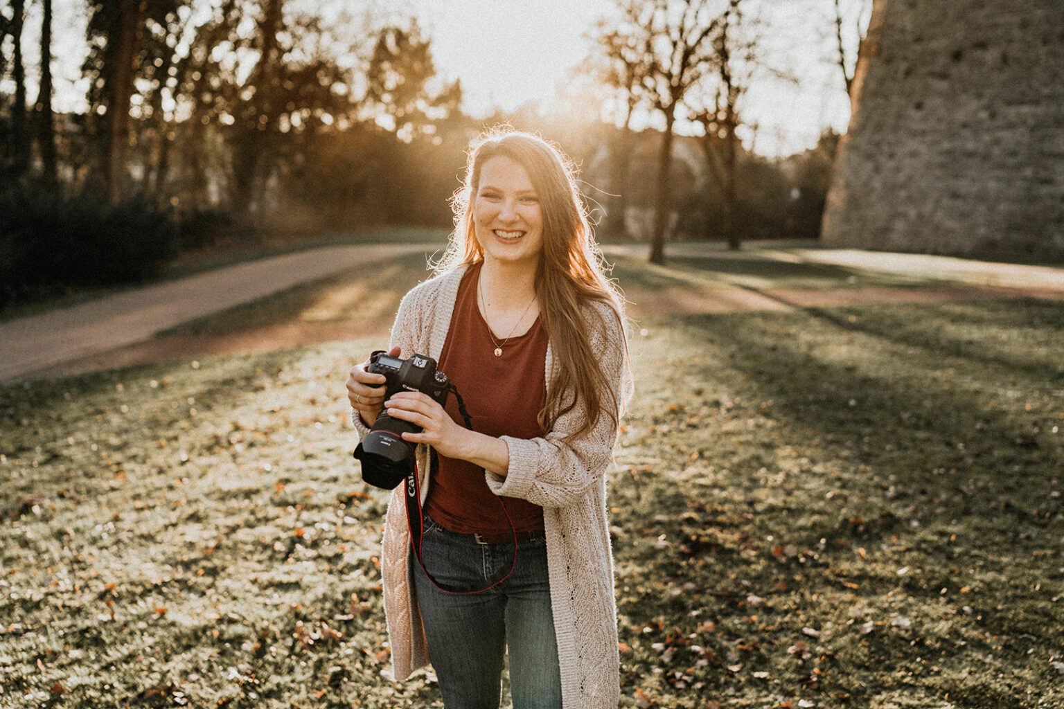 Portrait von Nadja Kuschel im Gegenlicht bei Sonnenuntergang vor der Sparrenburg in Bielefeld, sie hält ihre Kamera in der Hand und lacht