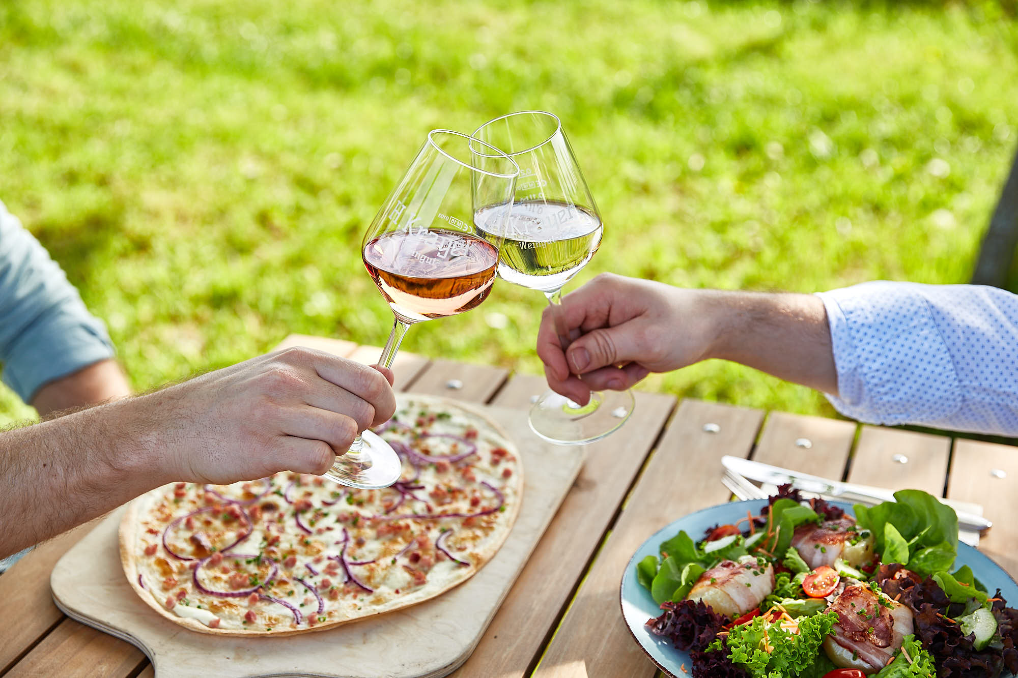 Foto von zwei Händen die an einem Tisch mit Essen mit zwei Weingläsern anstoßen